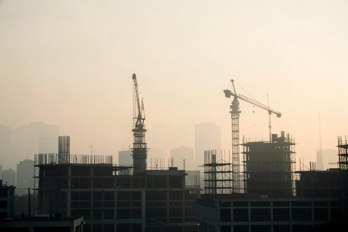 Construction cranes and scaffolding against a hazy skyline.